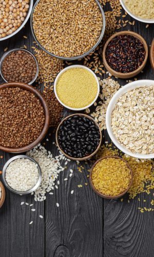 Different cereals, grains, seeds, groats, legumes and beans in bowls, top view of raw porridge collection on black wooden background with copy space